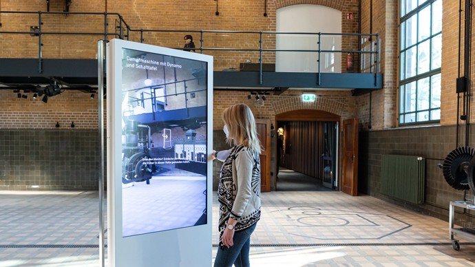 Eine Frau steht an einem großen Bildschirm im ehemaligen Maschinenhaus.